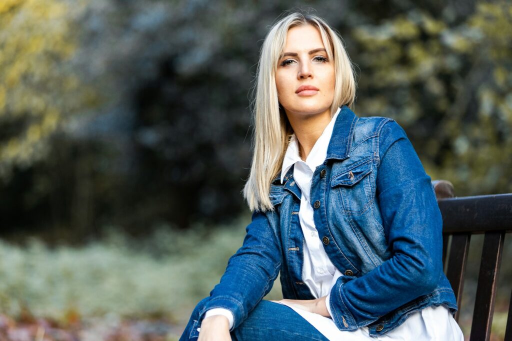 woman in blue denim jacket sitting on brown wooden bench during daytime
