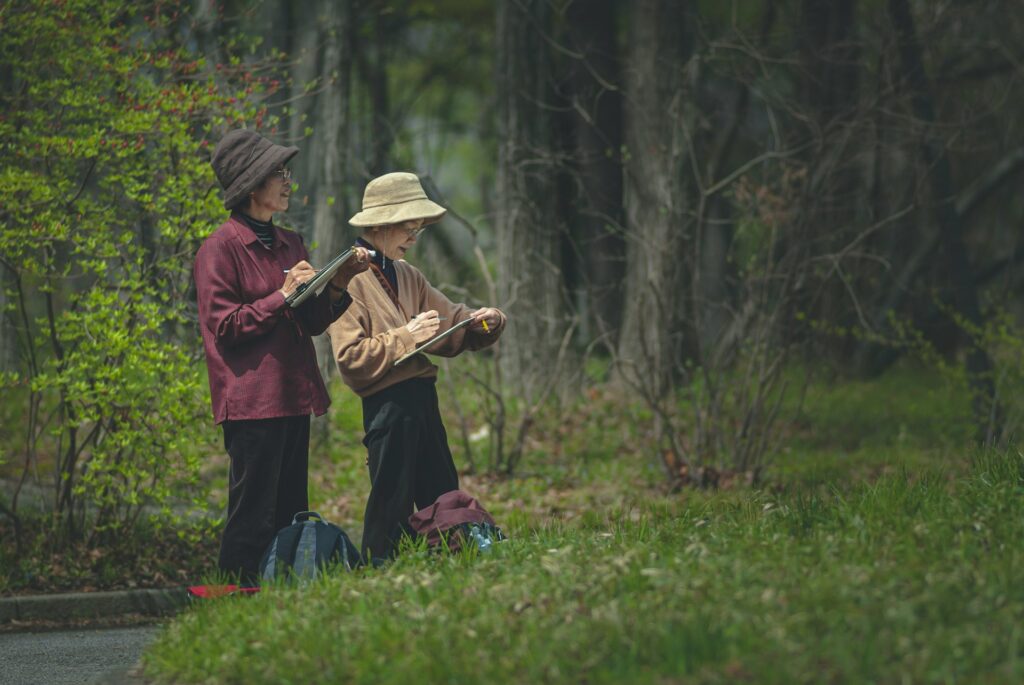 woman in red jacket and blue pants carrying baby in brown jacket on green grass field
