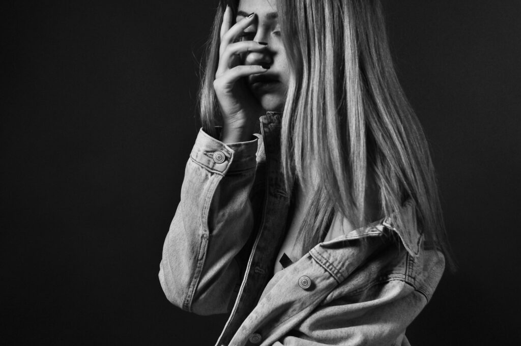 woman in denim jacket covering her face with her palm
