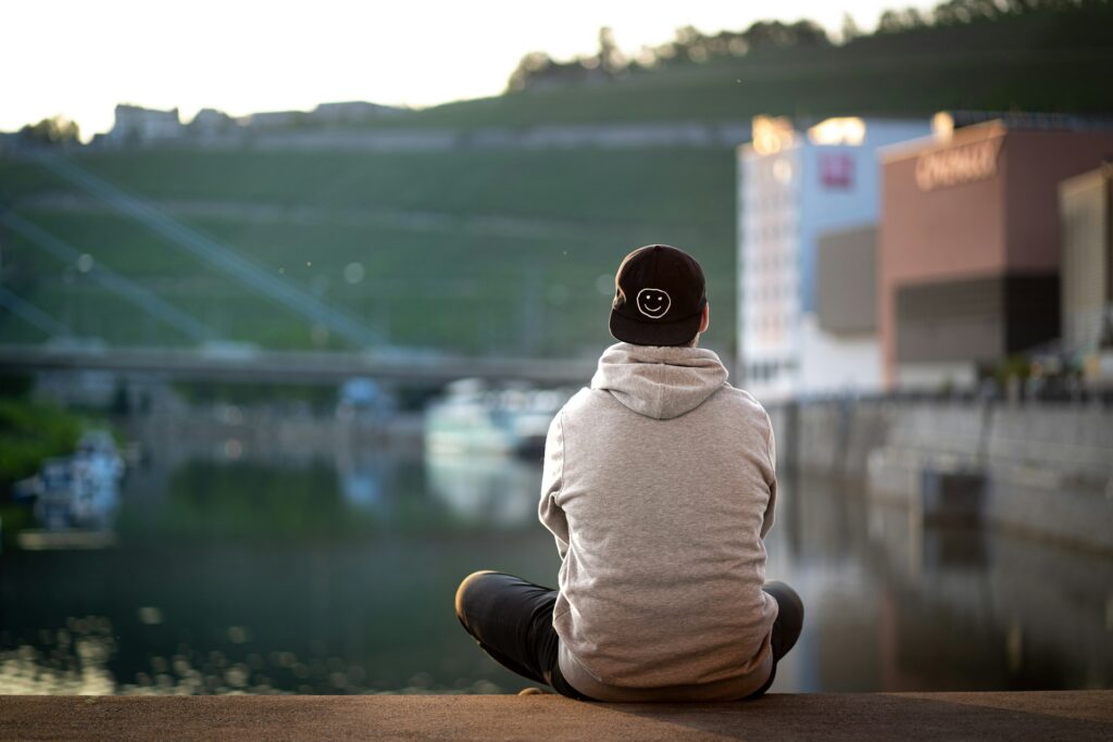man in gray hoodie sitting on brown concrete surface
