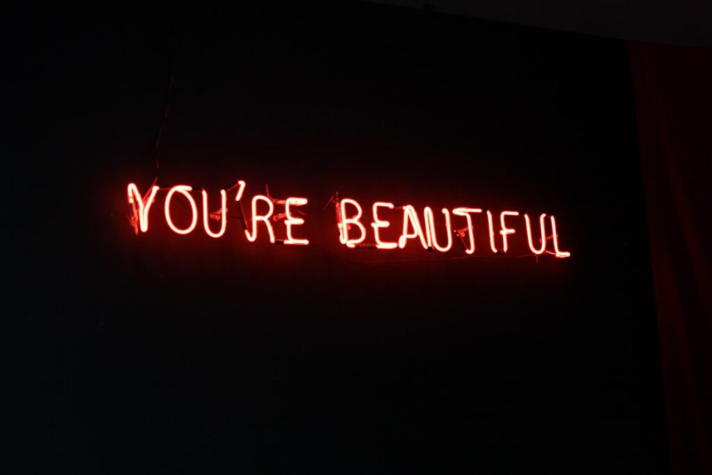 Red neon sign reading "YOU'RE BEAUTIFUL" glowing against dark background.