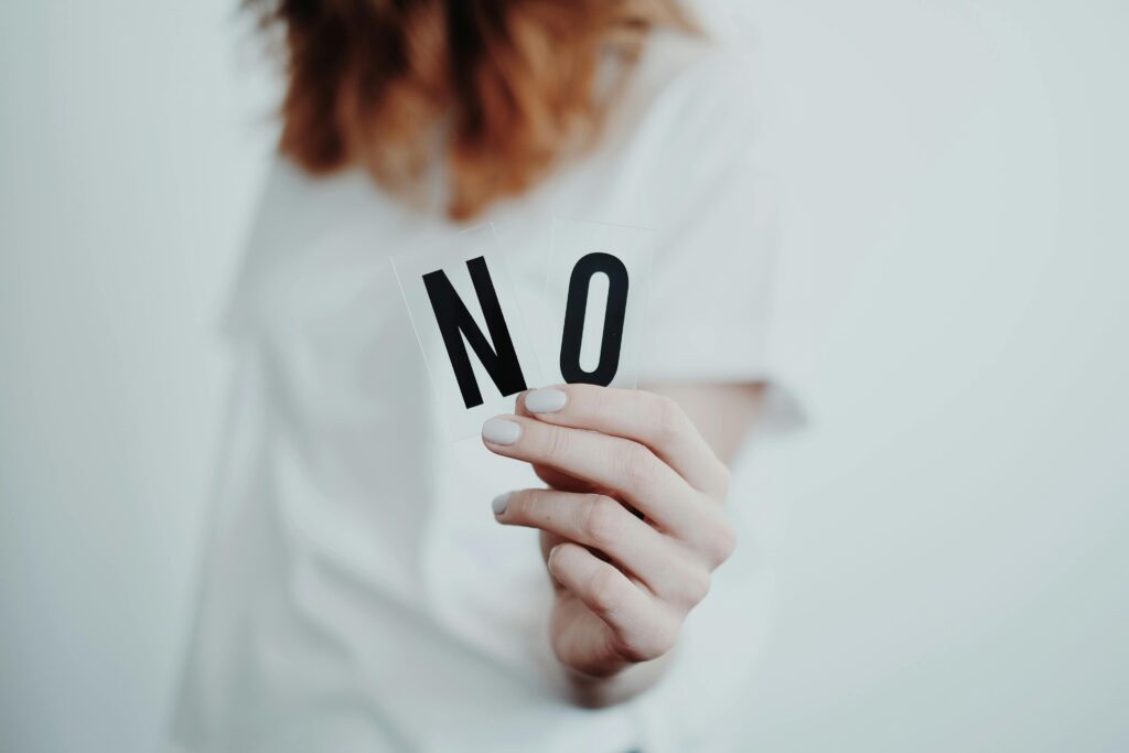 Person in white sweater holding small sign that reads "NO."