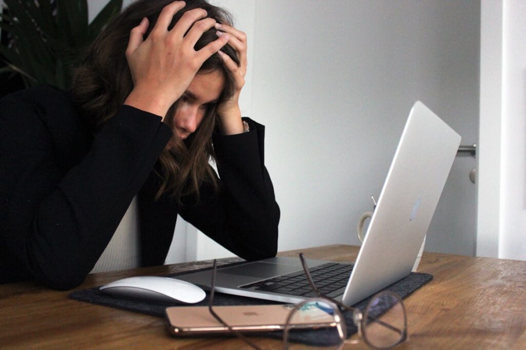 Woman with hands on head showing stress while working at laptop.