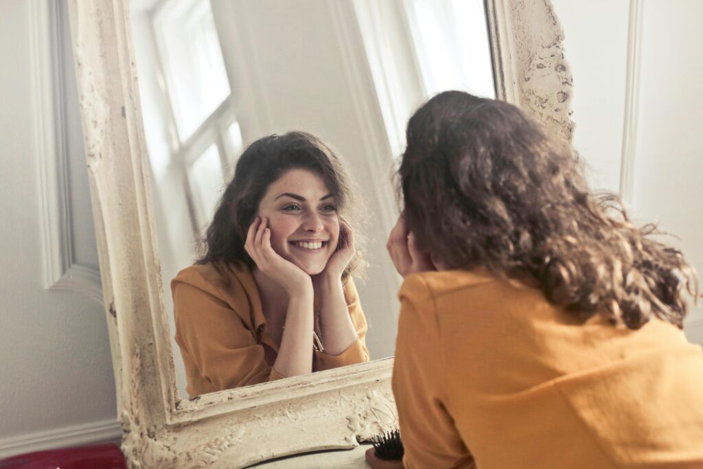 Woman smiling warmly while looking at herself in an ornate mirror.