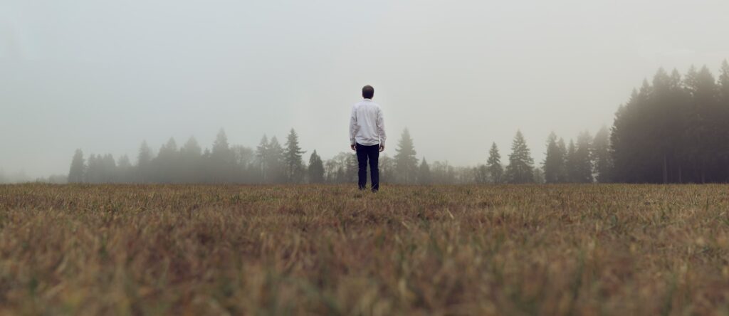 man standing in front of forest with fog
