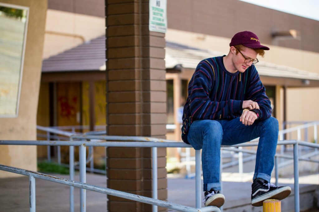 man wearing black sweater and blue jeans sitting on grey railings