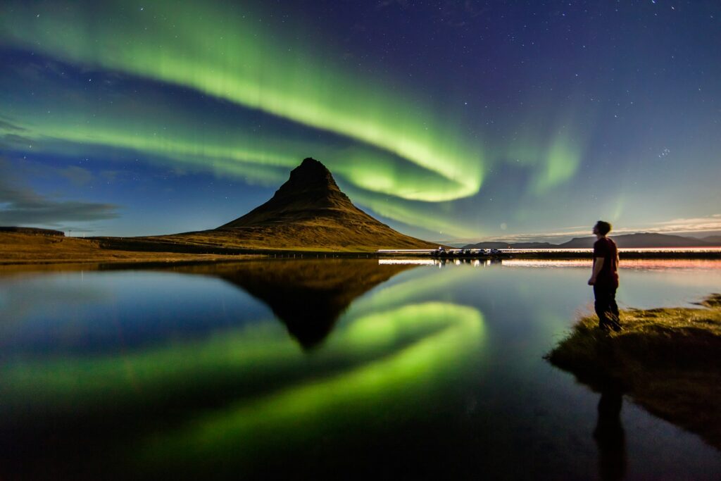man standing beside the body of water with Aurora lights in the sky
