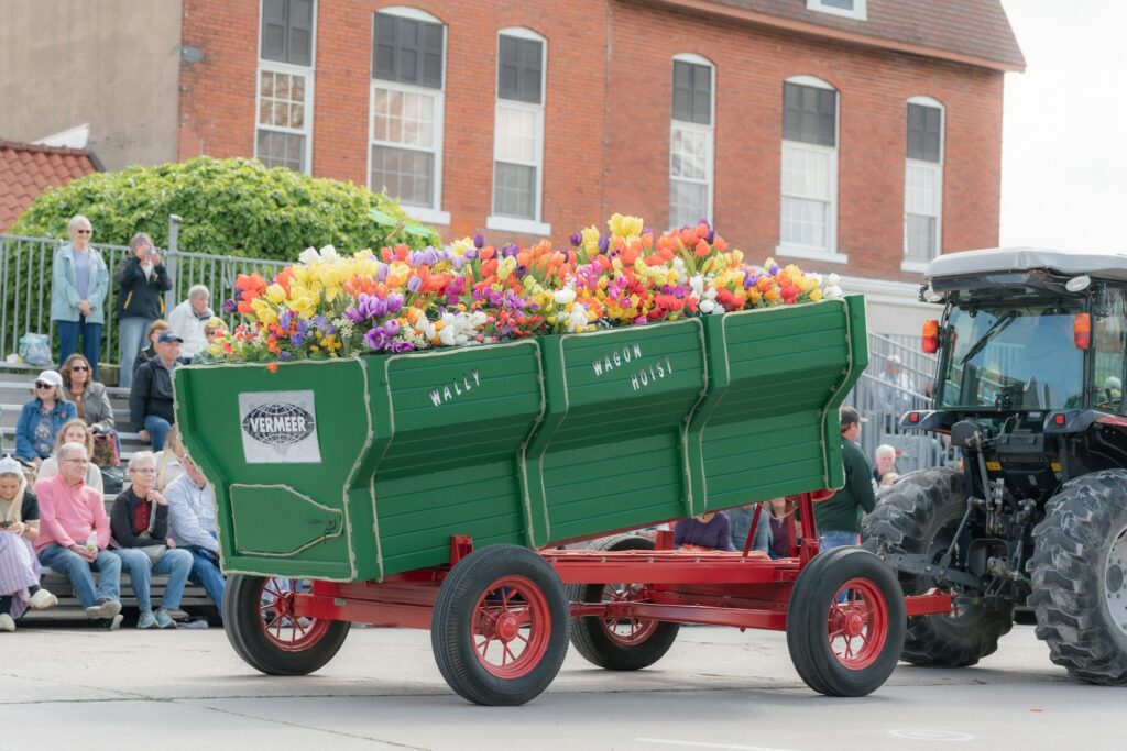 A tractor pulls a cart overflowing with flowers.
