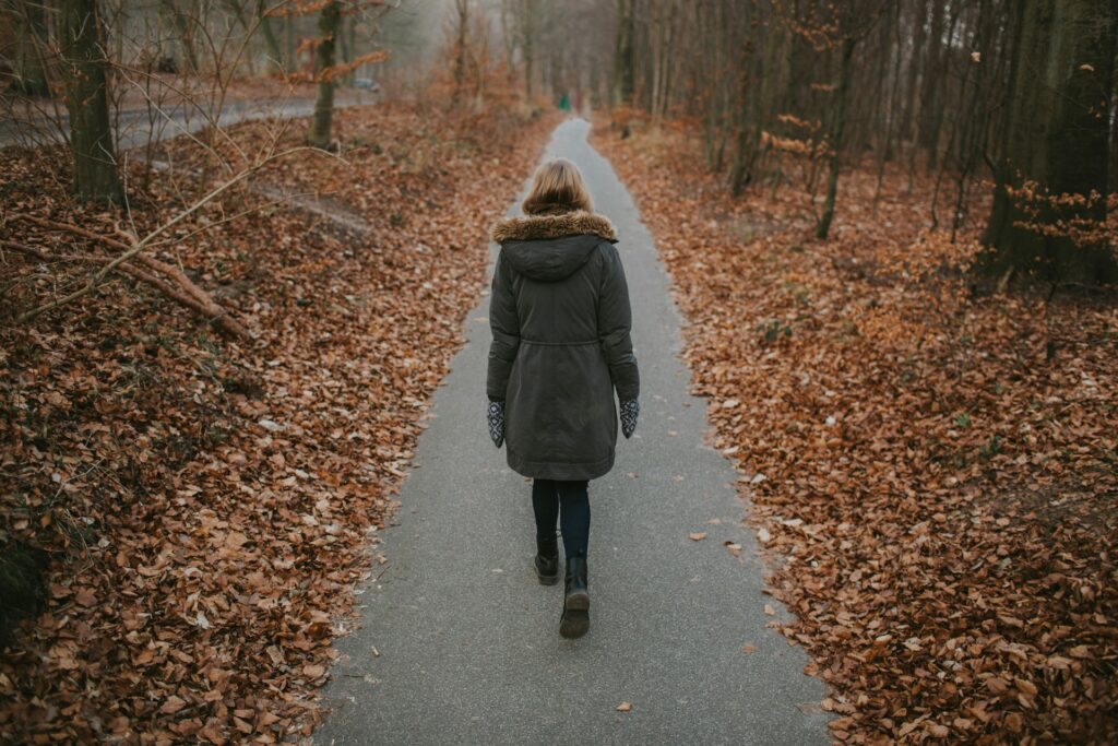 women walking on pathway surrounded by dried leaves
