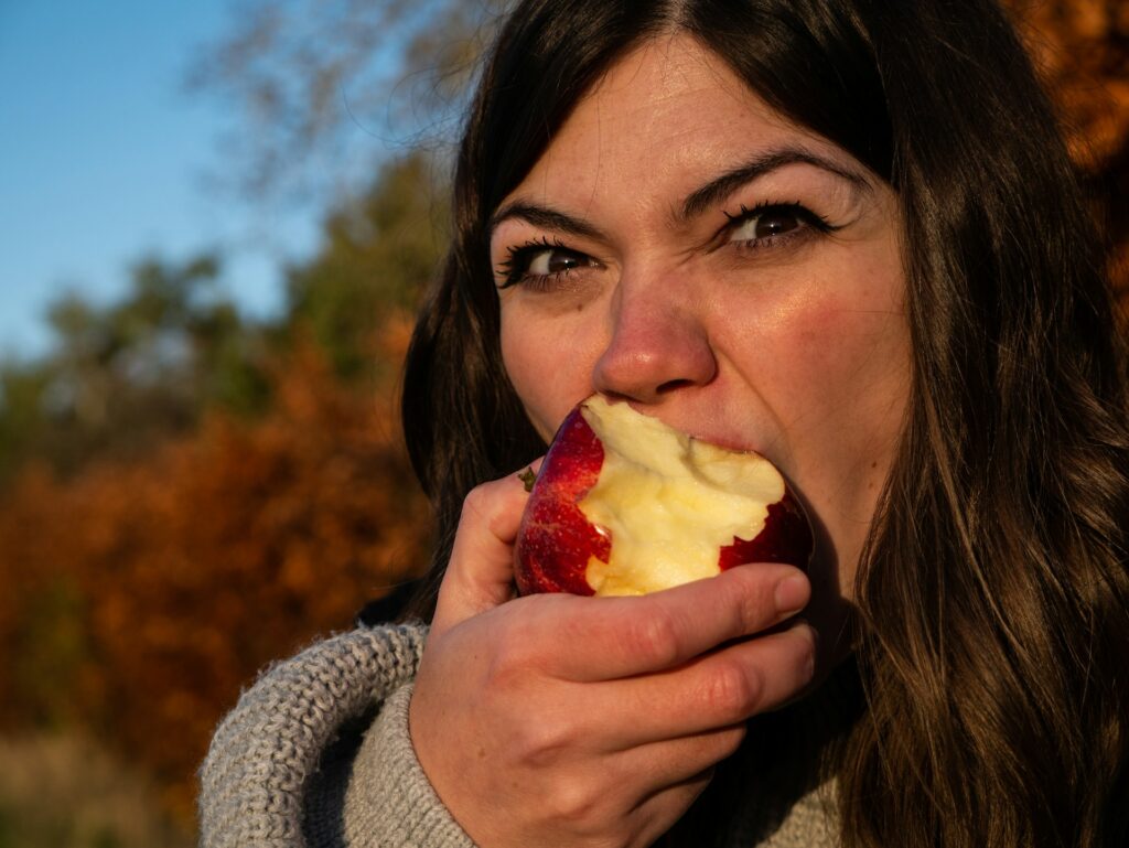 woman in gray sweater holding sliced of apple

