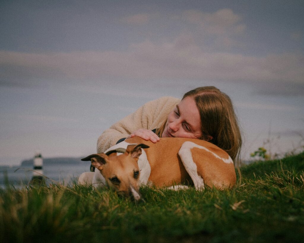a woman laying in the grass with a dog
