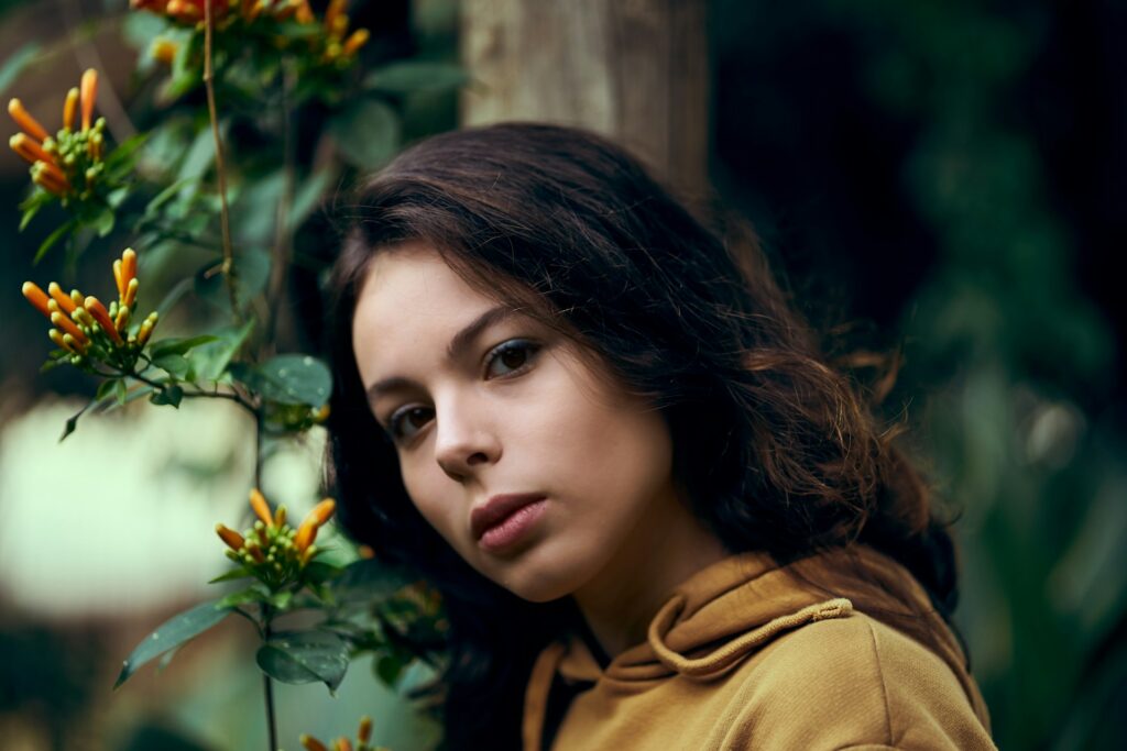 woman in brown coat standing near green plant
