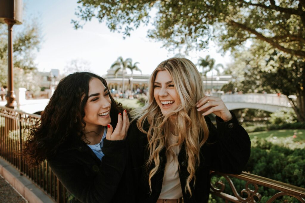 2 women smiling and standing near trees during daytime
