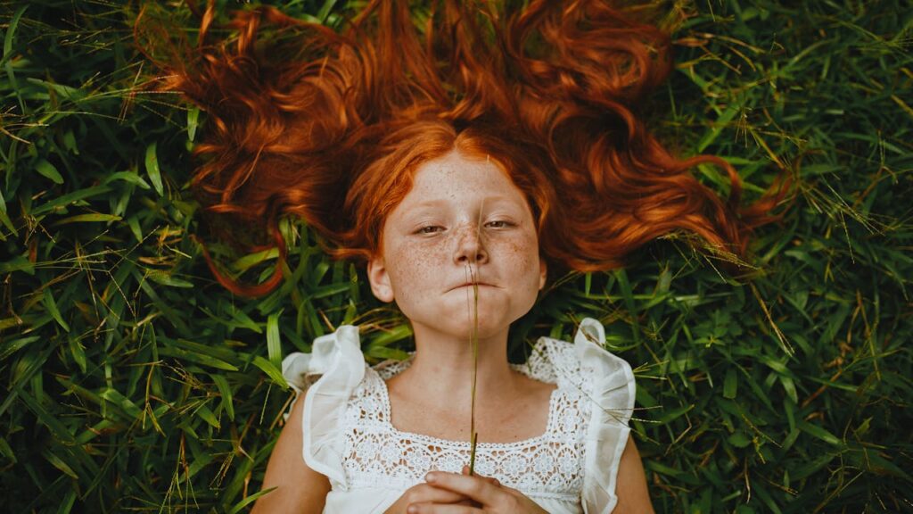 Girl Holding Plant While Lying on Grass
