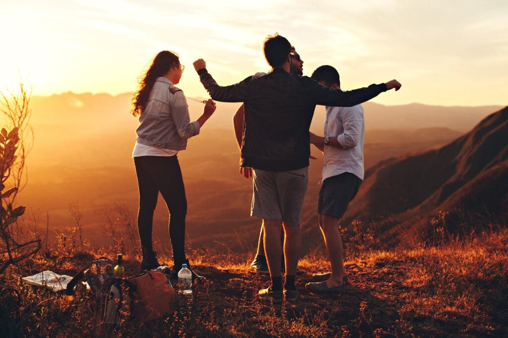 Four Person Standing at Top of Grassy Mountain
