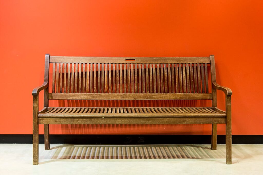A Brown Wooden Bench in Front of an Orange Wall
