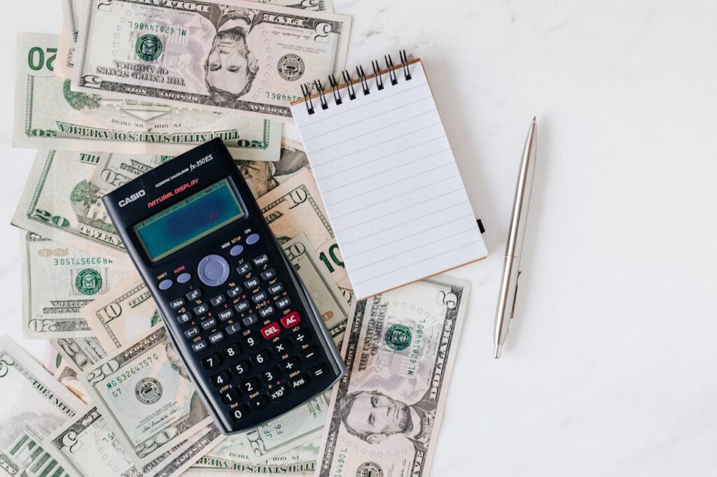 Calculator and Notepad placed over Stack of Paper Bills
