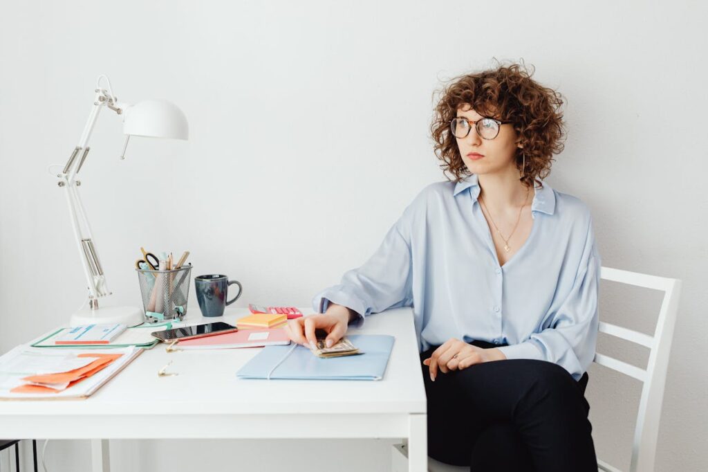 Woman in Blue Long Sleeve Shirt Sitting Sitting at Table Holding Money
