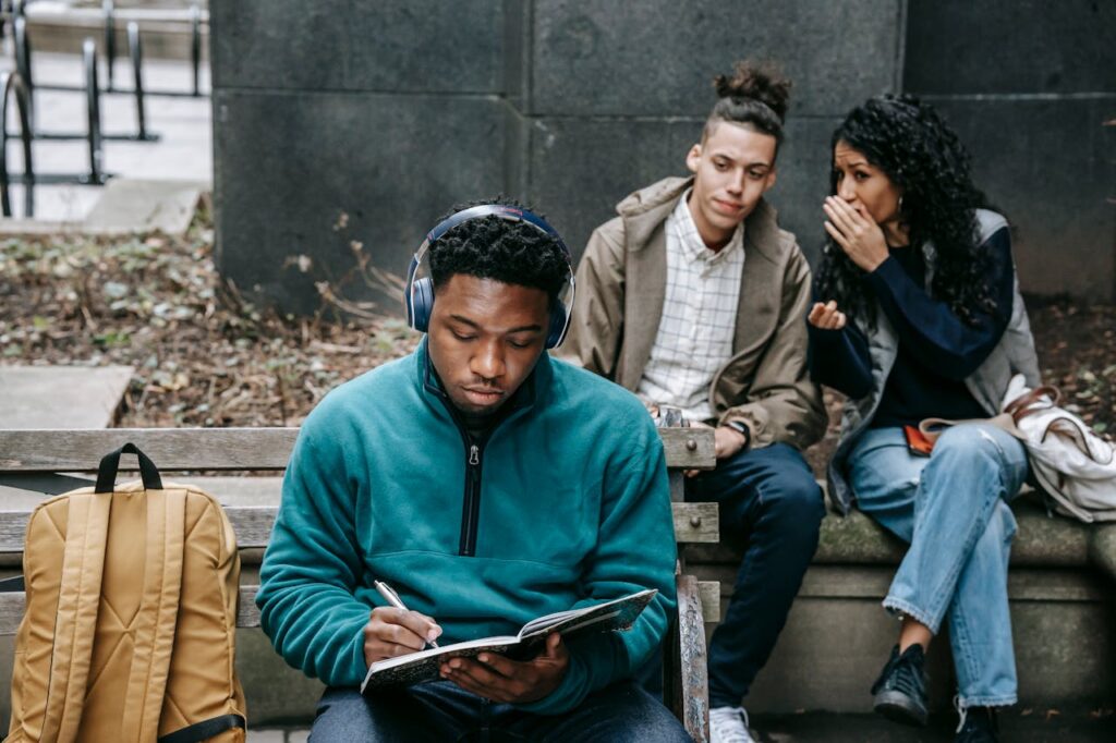 Multiracial students gossiping about black man with notepad
