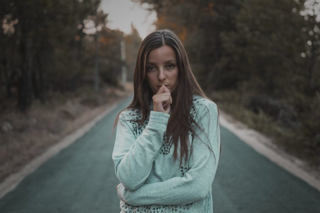 Photo of Woman Standing in The Middle of a Road Near Trees

