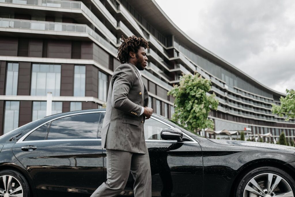 Man in Gray Suit Walking Beside Black Car
