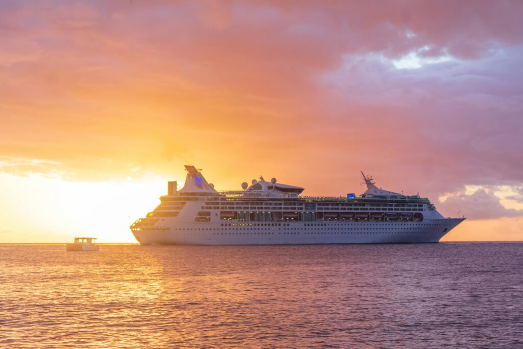  a large cruise ship at sea, with a smaller vessel nearby, set against a vibrant sunset sky. 