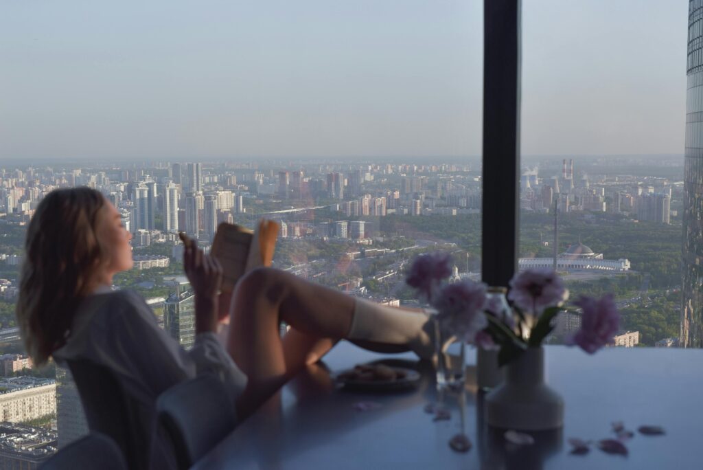 Woman Reading a Book on the Dining Table Inside the Apartment
