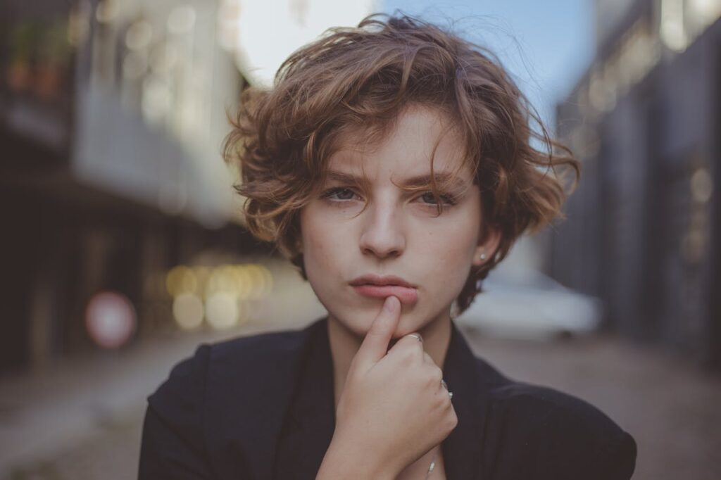 Selective Focus Portrait Photo of Woman Posing with Her Thumb Below Her Lip

