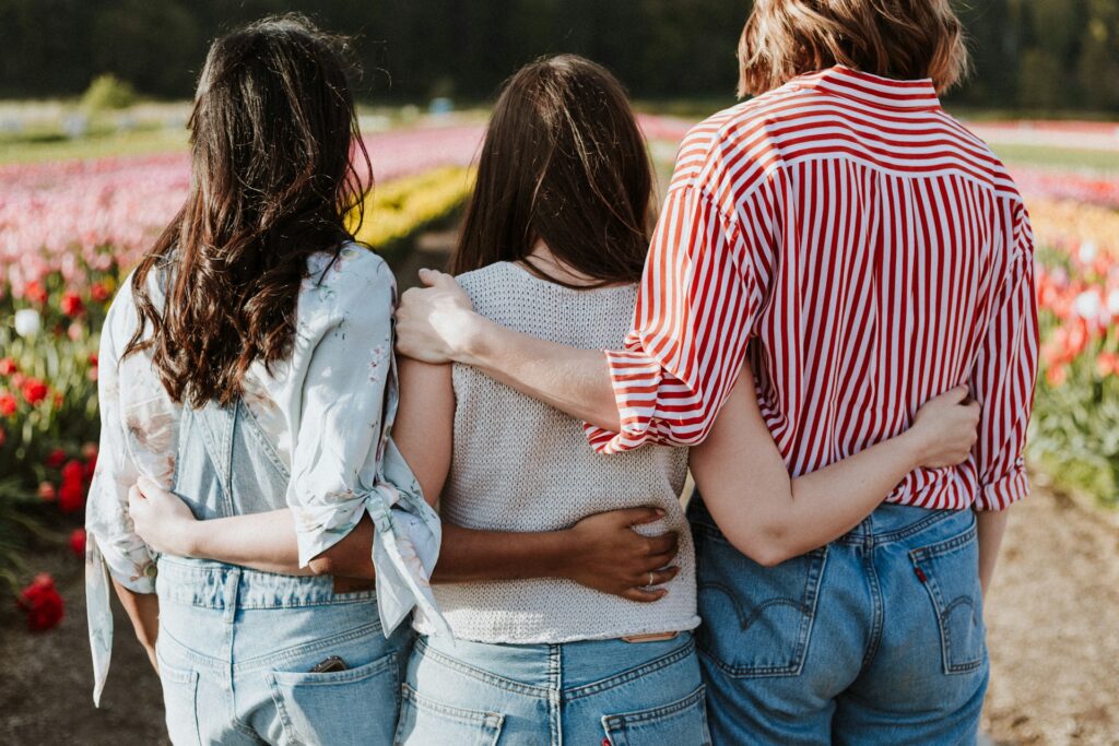 three women holding hand in front of flower garden
