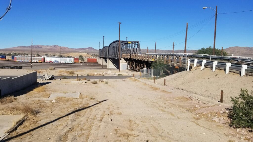 a train crossing a bridge over a dirt road
