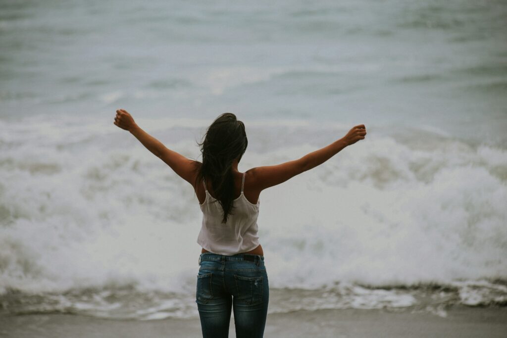 woman in white spaghetti strap top standing on the seashore
