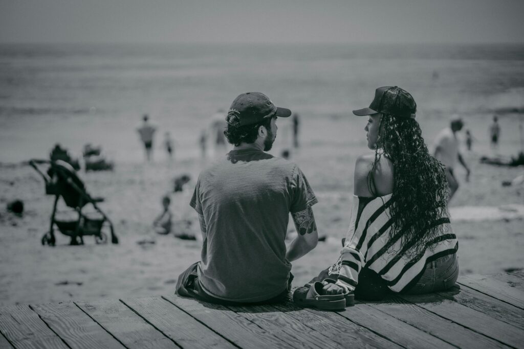 a man and a woman sitting on a pier looking at the beach

