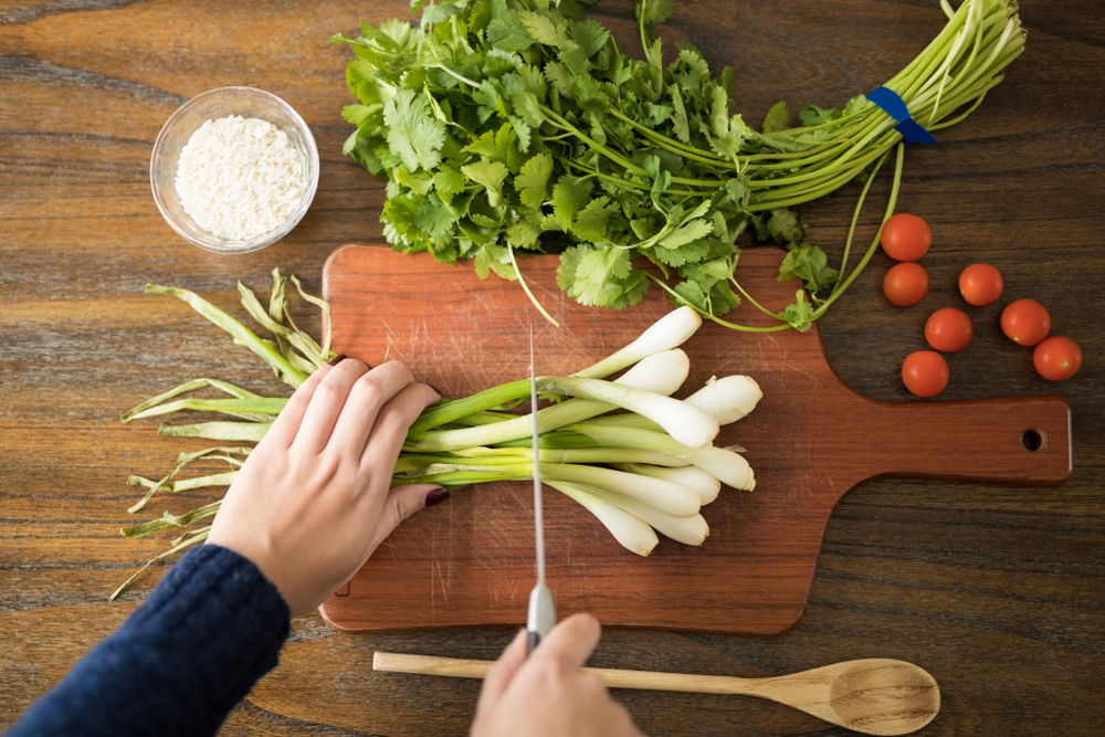 Point of view of woman cutting fresh vegetables on chopping board in kitchen