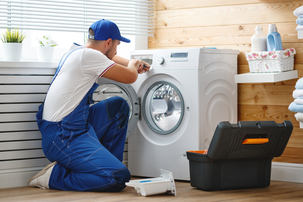 working man plumber repairs a washing machine in laundry