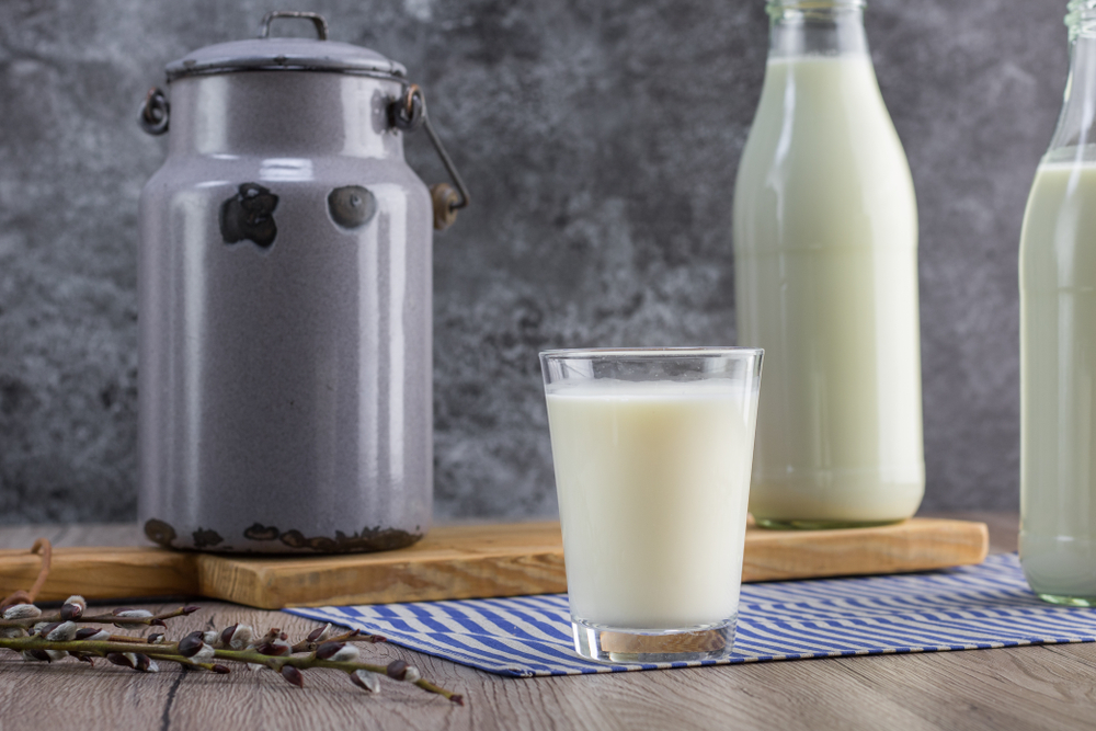 Detail on a glass jar with fresh unpasteurized milk on wooden board
