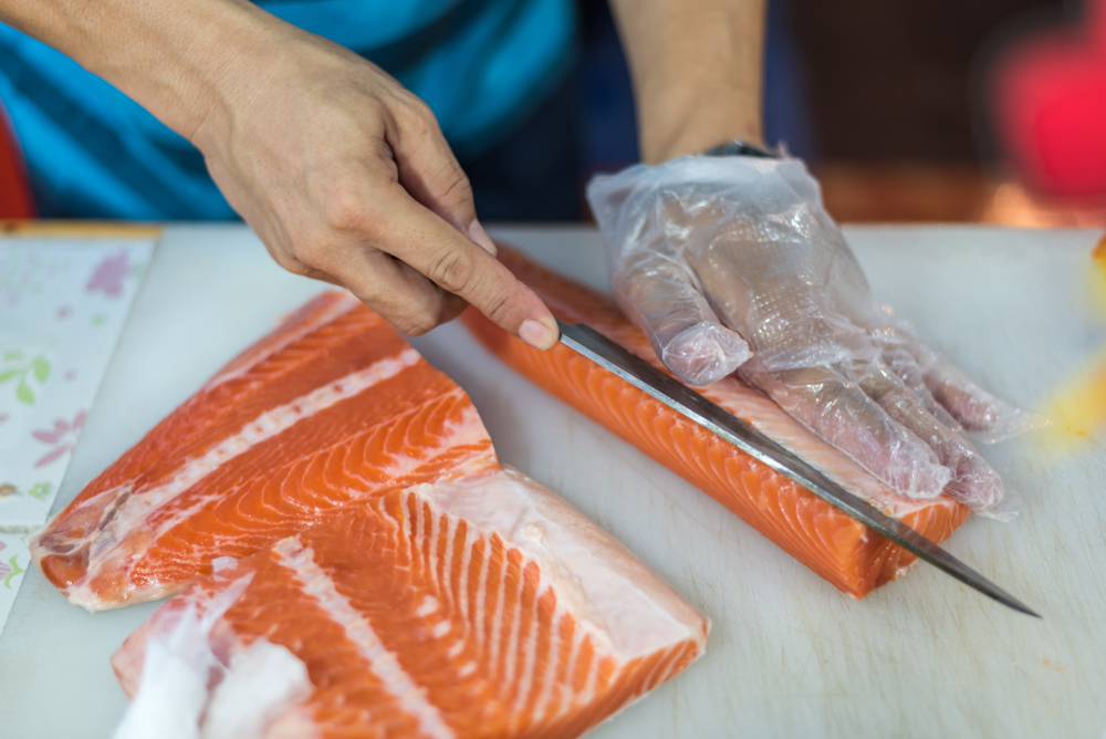 Asian chef slice salmon by knife on boad for japanese food delicacy consisting sashimi salmon of very fresh raw salmon fish sliced into thin pieces serving with radish sliced in japanese restaurant