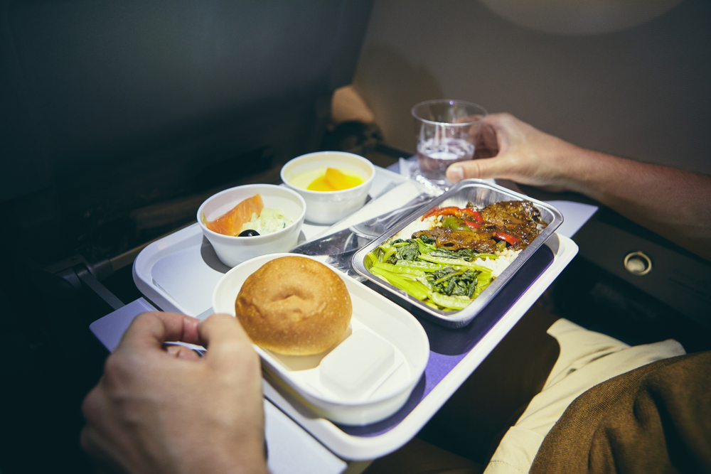 Traveling by airplane. Passenger enjoying dinner in economy class during long haul flight.
