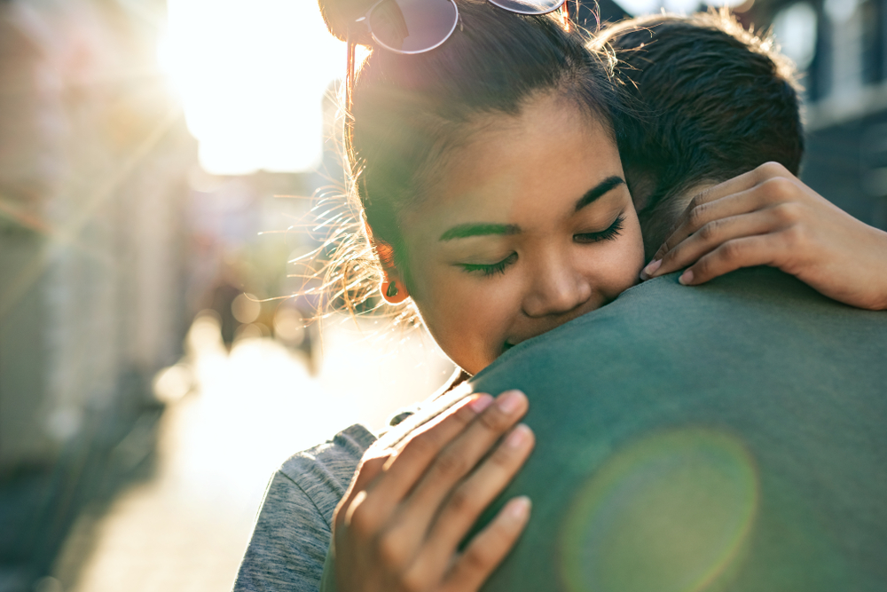 Young woman with her eyes closed hugging her boyfriend while standing together on a city street in the late afternoon