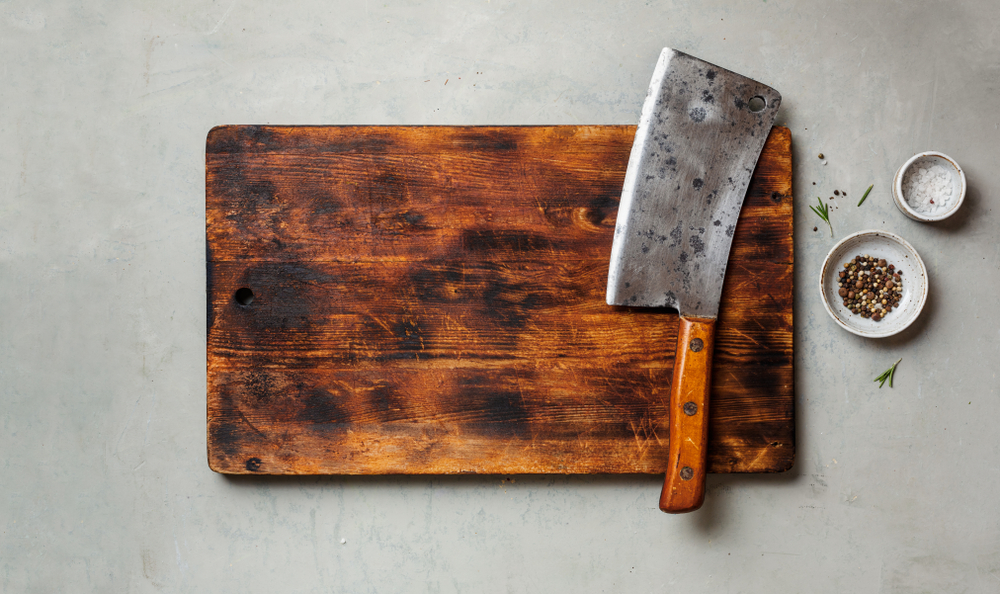 Vintage Meat cleaver on a empty old dark wooden cutting Board. Top view, space for text.