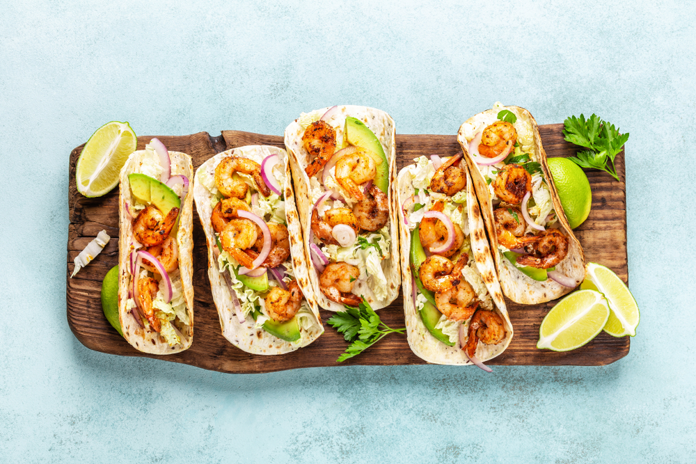 Shrimp tacos. Seafood fajitas with cabbage, onion, parsley in tortillas served on wooden cutting board