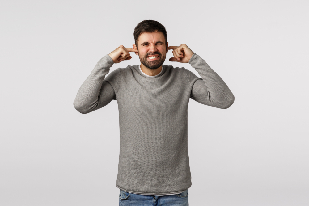 Distressed and disturbed guy bothered by loud neighbour, grimacing, clench teeth and squinting, shut ears, plug fingers unwilling hear awful sound, telling turn-off music, standing white background
