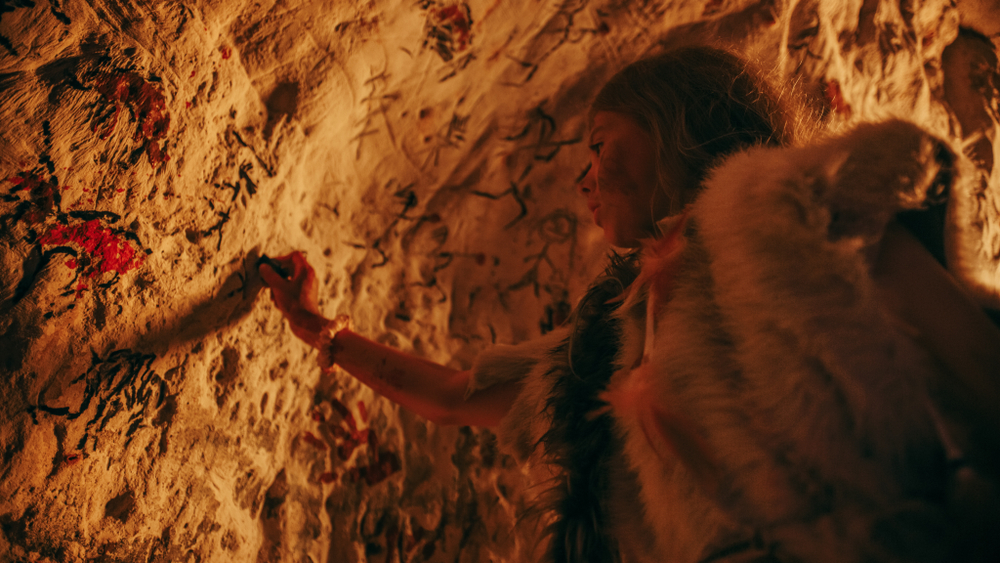 Primitive Prehistoric Neanderthal Child Wearing Animal Skin Draws Animals and Abstracts on the Walls at Night. Creating First Cave Art with Petroglyphs, Rock Paintings Illuminated by Fire. Low Angle