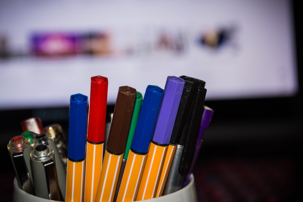 A selective focus of pens with colored caps in front of a computer screen
