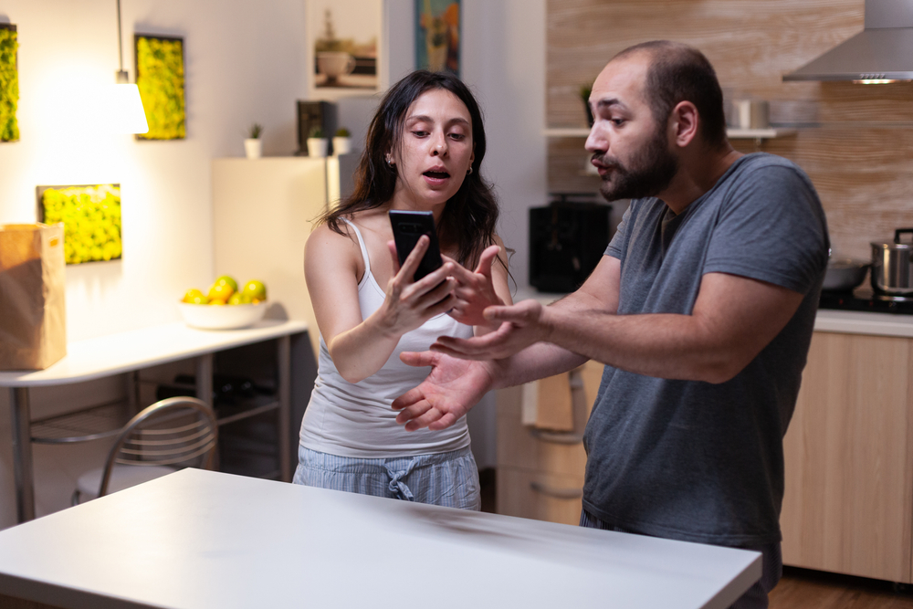 Caucasian man caught cheating by jealous wife looking at secret messages on smartphone. Couple fighting and yelling because of infidelity and trust issues. Marriage crisis, conflict
