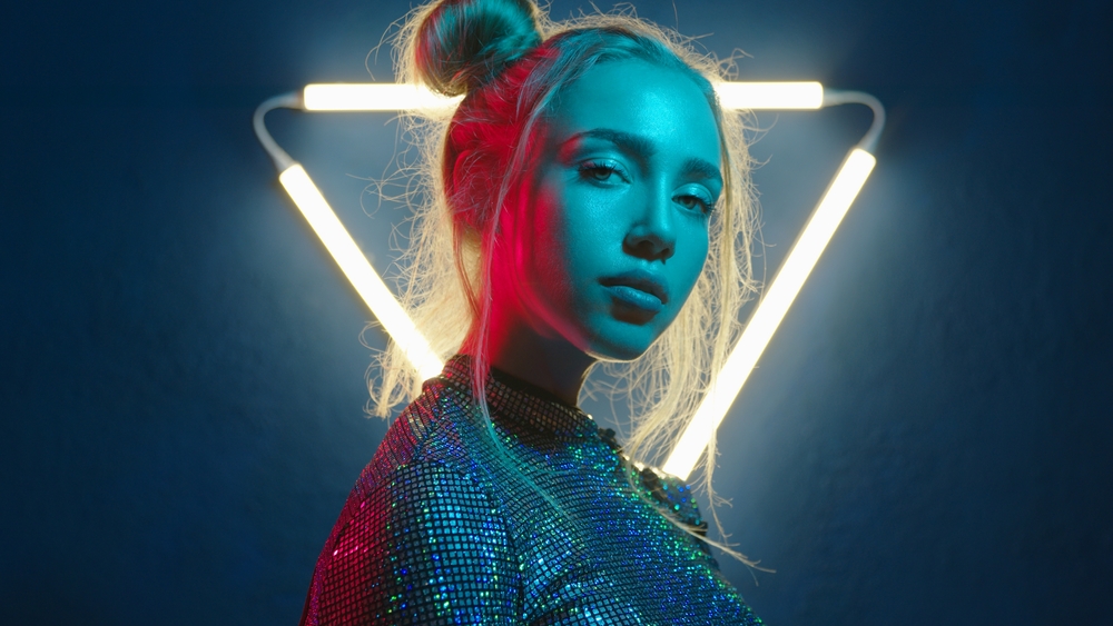 Young woman looking at the camera in the neon light of the club. Camera zoom. Portrait of a beautiful futuristic girl close-up. Lady in multicolor glow.