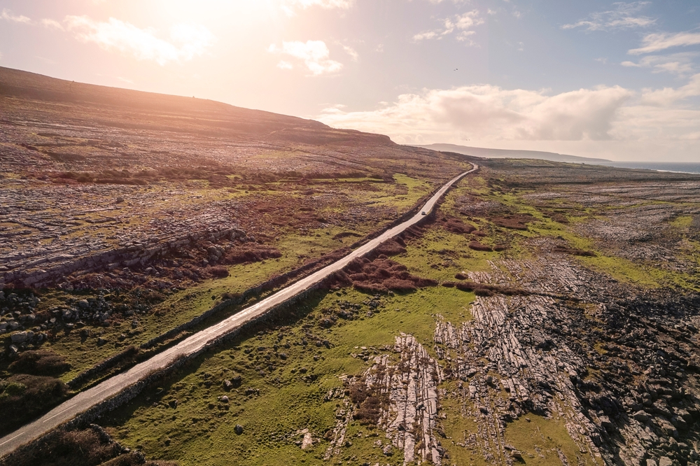 Small road by a mountain in Burren, Ireland. Wild Atlantic way. Beautiful scenery with rough stone surface and green grass hill. Nobody, Warm sunny day. Travel and tourism area.