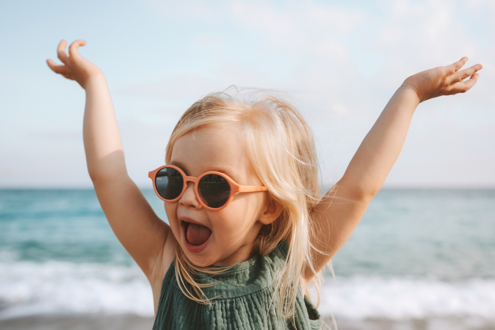 Funny kid girl playing outdoor surprised emotional child in sunglasses 3 years old baby raised hands family vacations
