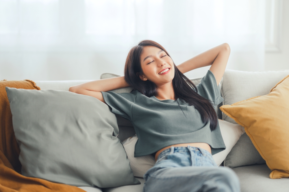 Relaxed young asian woman enjoying rest on comfortable sofa at home, calm attractive girl relaxing and breathing fresh air in home, copy space.
