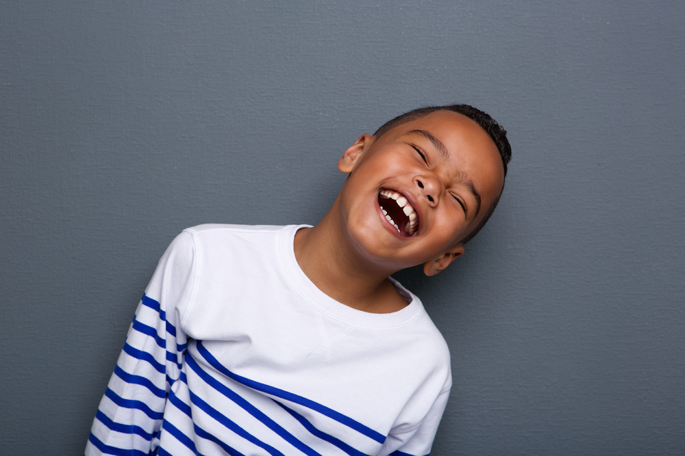 Close up portrait of a happy little boy smiling on gray background
