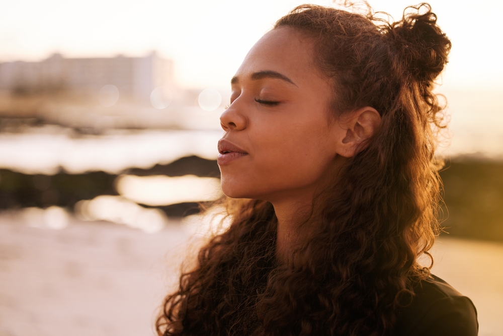 The universe speaks when you stop and listen. Shot of an attractive young woman sitting alone on a mat and meditating on the beach at sunset.
